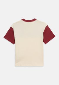 Μπεζ κοντομάνικο μπλουζάκι με σκουροκόκκινα μανίκια και γιακά σε αντίθεση, εμφανίζεται από πίσω σε απλό φόντο.