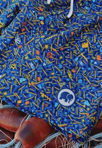 Tela azul con un patrón abstracto colorido que incluye remolinos, zigzags e íconos; presenta un logo de elefante azul redondo.