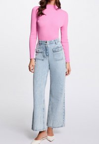 Top lungo a maniche ribbed rosa abbinato a jeans a gamba larga azzurri a vita alta con due tasche frontali e una texture liscia.
