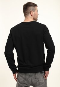 Felpa nera con colletto a girocollo, maniche lunghe e polsini a costine. Presenta una texture liscia e una vestibilità leggermente sagomata in vita.