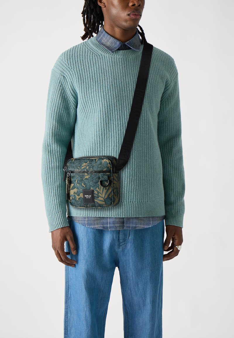 Maglione verde a coste, camicia di denim blu e pantaloni azzurri chiari. Borsa a tracolla con motivo floreale, strap nera e zip.