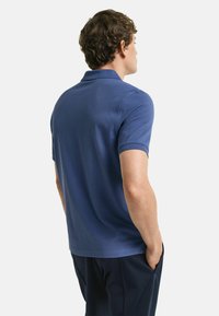 Kortärmad polo i mörkblå bomull, med klassisk krage och slät textur. Bakifrån visar den en figurnära silhuett och en minimalistisk design.