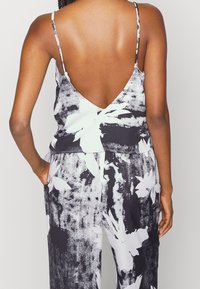 Top floreale in bianco e nero con scollatura a V profonda, spalline sottili e vestibilità rilassata. Tessuto liscio con dettagli di texture sottili.