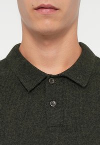 Zelena pletena pamučna majica polo s teksturiranim materijalom, s kragnom i dva tamna gumba na području vrata.