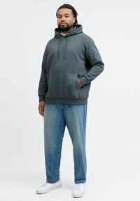 Mørkegrå hettegenser med kengurulomme, snøring i hetten og ribbestrikkede mansjetter, kombinert med løstsittende lyseblå denimjeans og hvite joggesko.