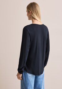 Svart långärmad topp med en avslappnad passform, jämn textur och lätt gathered ärmar, kombinerad med ljusblå denimjeans.