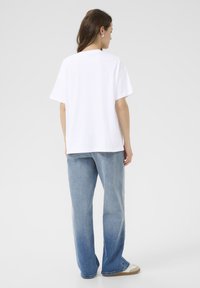 T-shirt blanc oversize à manches courtes, associé à un jean taille haute délavé bleu. Tissu uni, coupe décontractée, sans motifs visibles.