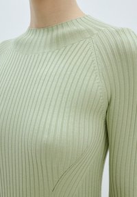 Haut en maille verte côtelée avec un col montant et des détails d'épaule sans couture, présentant une texture subtile et des éléments de design ajustés.