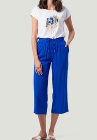 Top blanco de manga corta con arte lineal floral; pantalones cortos sueltos y azules con cintura elástica ajustable; sandalias planas.