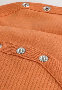 Tissu orange à côtes avec des boutons-pression en argent. Texture lisse avec des surpiqûres contrastées. Détail du col arrondi visible.