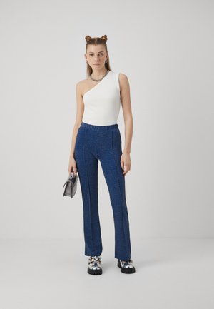 Λευκή τοπ ένα ώμο, συνδυασμένη με μπλε σπιρτόζικα καμπάνα παντελόνια, με ελαστική μέση και ασημένιο κολιέ κατά προτίμηση. Τα αξεσουάρ περιλαμβάνουν μια μικρή γκρι τσάντα.