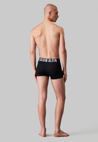 Schwarze Boxer-Briefs mit einem weißen Calvin Klein-Logo am Bund, die ein figurbetontes Design und glattes Material zeigen. Von hinten betrachtet.