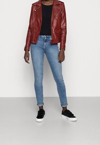 Punainen nahkainen moottoripyöräjacketti, jossa on hopeiset yksityiskohdat, yhdistettynä istuviin vaaleansinisiin farkkuihin ja mustiin liukuportaisiin tennareihin. Yksinkertainen, moderni muotoilu.