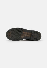 Suola di un stivale in gomma nera con profonde scanalature, caratterizzata dal logo Dr. Martens e da testo nella zona del tallone.