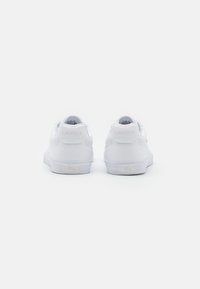 White leather sneakers with a low-top design, featuring a textured rubber sole, embossed logo on the heel, and minimalistic stitching details.