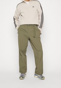 Ljusbeige zip-up sweatshirt med svarta ränder, kombinerad med olivgröna lätta byxor med bälte och sidofickor.