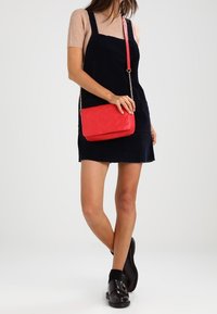 Borsa a tracolla intrecciata rossa con tracolla a catena dorata, abbinata a un vestito in velluto a coste blu scuro e stivali neri robusti alla caviglia.