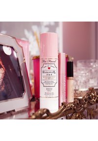 Too Faced Hangover 3-in-1 Herstelprimer en Setting Spray in een roze en witte fles met een decoratief etiket. 120 ml, olie-vrij.