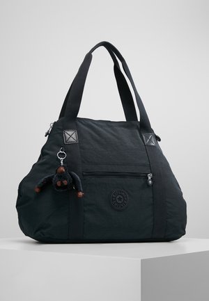Bolso de nylon negro con doble asa, bolsillo frontal con cremallera, parche redondo con logo y un pequeño llavero de mono de peluche colgando de la correa.