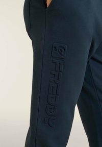 Pantalones jogger en color azul marino, confeccionados con una tela elástica, que cuentan con un logo texturizado en un color contrastante a lo largo del lado de la pierna izquierda.