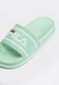 Sandal in verde menta realizzato in gomma liscia, con una ampia banda bianca che presenta il logo del marchio e un accento rosso. Suola piatta e strutturata.