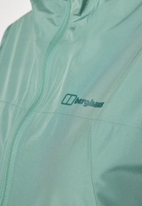 Giacca leggera e resistente all'acqua di colore teal, con chiusura a zip, colletto rialzato e logo ricamato. Texture liscia con una leggera lucentezza.