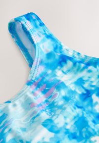 Uimahupun olkaimet, joissa sinisen ja turkoosin tie-dye-kuvio, jossa on ripaus purppuraa. Valmistettu pehmeästä, joustavasta kankaasta; pyöreä päänti.