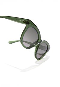 Ochelari de soare supradimensionați verzi, cu ramă geometrică, lentile întunecate și brațe conice. Numele mărcii "HAWKERS" este imprimat pe tâmpla stângă.