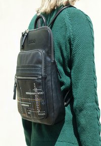Mochila de cuero negra con un bolsillo frontal texturizado que presenta patrones de costura multicolores, correas ajustables y un asa superior.