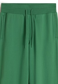 Groene sweatpants van een gladde stof hebben een elastische tailleband met een trekkoord, zijzakken en een losse pasvorm.
