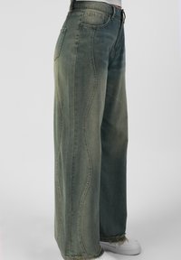 Široke jeans hlače iz zbledelog zelena denima s kontrastnim ukrasnim šavovima. Pofrane rubove i standardni žepovi zaokružuju dizajn.