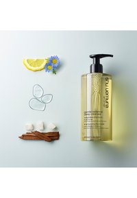 Bouteille en plastique transparente de shampoing jaune avec une pompe noire, entourée de rondelles de citron, de fleurs, de gouttes d'huile, de cubes de sucre et d'un bâton de cannelle.