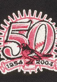 Black fabric patch featuring white and pink embroidery, displaying the number "50" and a bird, with "1954" and "2004" below.