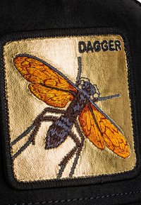 Cappello di tessuto nero con una toppa ricamata in oro che rappresenta un dettagliato insetto con ali arancioni e corpo scuro, etichettato "DAGGER".