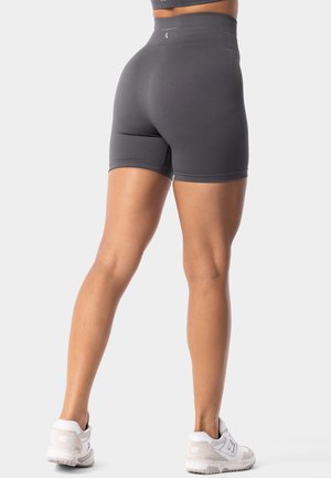 Šedé šortky s vysokým pasem vyrobené z elastické tkaniny, s hladkou texturou a těsným střihem, zkombinované s bílými sportovními botami.