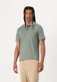 Polo a maniche corte in cotone verde chiaro, con colletto, patta con bottoni e vestibilità rilassata. Abbinato a pantaloni beige.