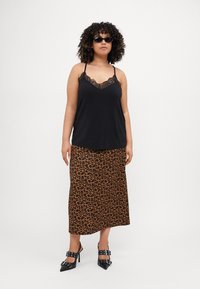 Schwarz mit Spitze besetztes Camisole, kombiniert mit einem Maxirock im Leopardenmuster. Model trägt schwarze spitze Absätze und Sonnenbrille, mit lockigem Haar.