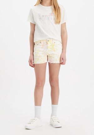 Hvid Levi's t-shirt med logo, kombineret med pastelfarvede tie-dye shorts i gul og orange. Har frynset kant og hvide sneakers med stropper.