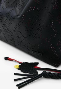 Mustast nahast kott, millel on lõigatud lillmustritega mustrid, punased ja kollased aktsendid ning dekoratiivsed rihmad. Tekstuuriga viimistlus ja elegantne disain.