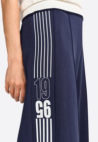 Pantalons de survêtement bleu marine avec des rayures blanches verticales et un grand graphique "1996". Taille élastique et texture de tissu douce.