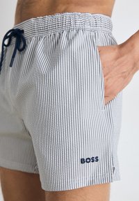 Calções de banho às riscas em azul claro e branco, com cintura elástica, cordão de aperto e logótipo bordado "BOSS" na coxa esquerda.