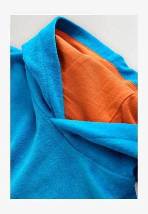 Modra kapuca iz frotirja z oranžno bombažno podlogo. Tkanina ima teksturirano površino, ki poudarja kontrast barv.