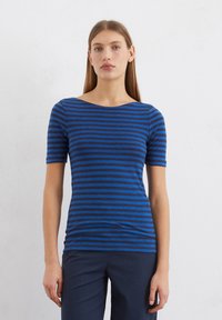 Blau- und marineblau gestreiftes T-Shirt mit einem Bootsausschnitt und kurzen Ärmeln, aus einem weichen Stoff gefertigt, kombiniert mit dunklen Hosen.