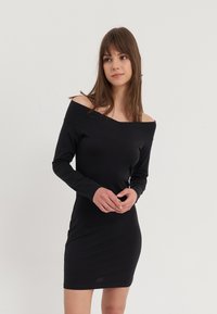 Robe noire décolletée avec des manches longues, silhouette ajustée et tissu doux. Présente un décolleté large et des détails de couture subtils.