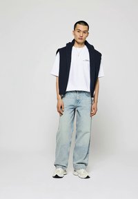 Himmlisch marineblaues ärmelloses Hoodie über einem weißen T-Shirt, kombiniert mit hellblauen Jeans und weißen Sneakers. Einfaches Design in einfarbigen Farben und lässiger Passform.