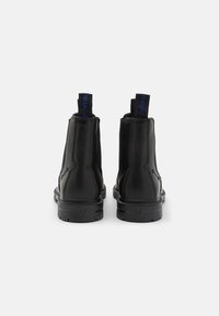 Botas de tobillo de cuero negro con un acabado brillante, tiradores y suelas de goma texturizadas; diseño minimalista con detalles de costura en los lados.