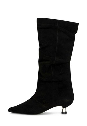 Bota de ante negra hasta la mitad de la pantorrilla con diseño holgado, puntera puntiaguda y tacón metálico corto de tipo kitten, sobre fondo blanco.