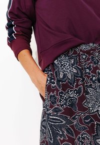 Sweatshirt bordeaux avec des accents bleu marine et des rayures blanches, associé à une jupe à motifs floraux présentant des détails bleu foncé et blancs.