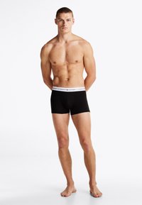 Sorte boxerbriefs med en hvit midjebånd som har "TOMMY HILFIGER"-logo. Stoffet ser glatt ut med en tettsittende passform.