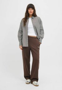 Maglietta a righe grigie e bianche, canottiera bianca, pantaloni sportivi marroni e sneakers argento. Vestibilità comoda con dettaglio della tasca frontale sulla maglietta.